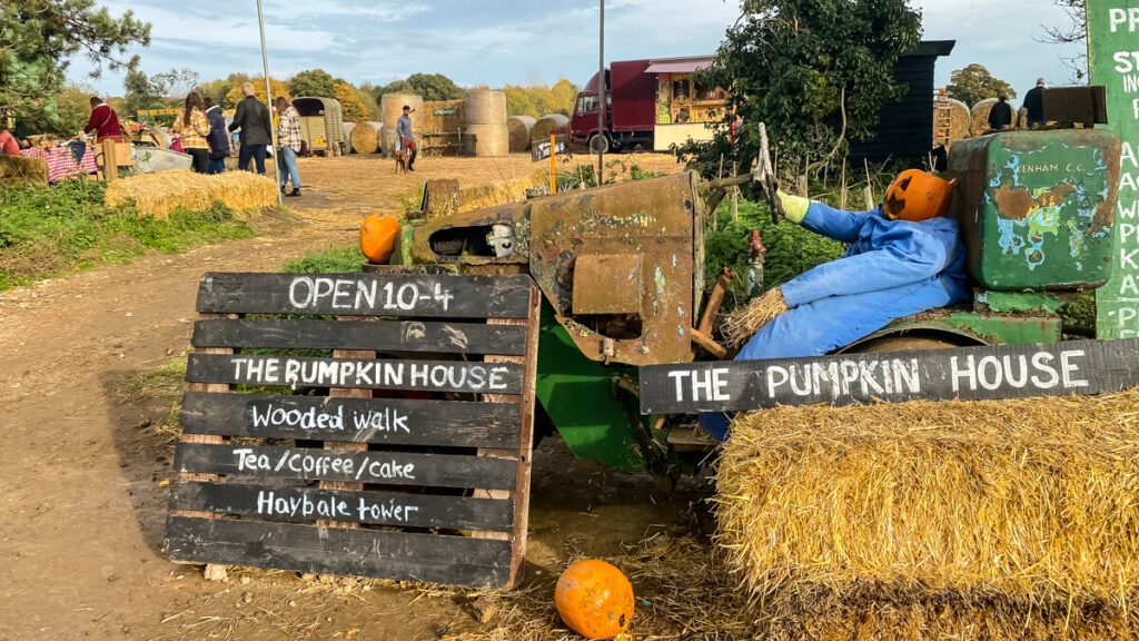 scarecrow with pumpkin on old tractor with sign about pumpkin house hours