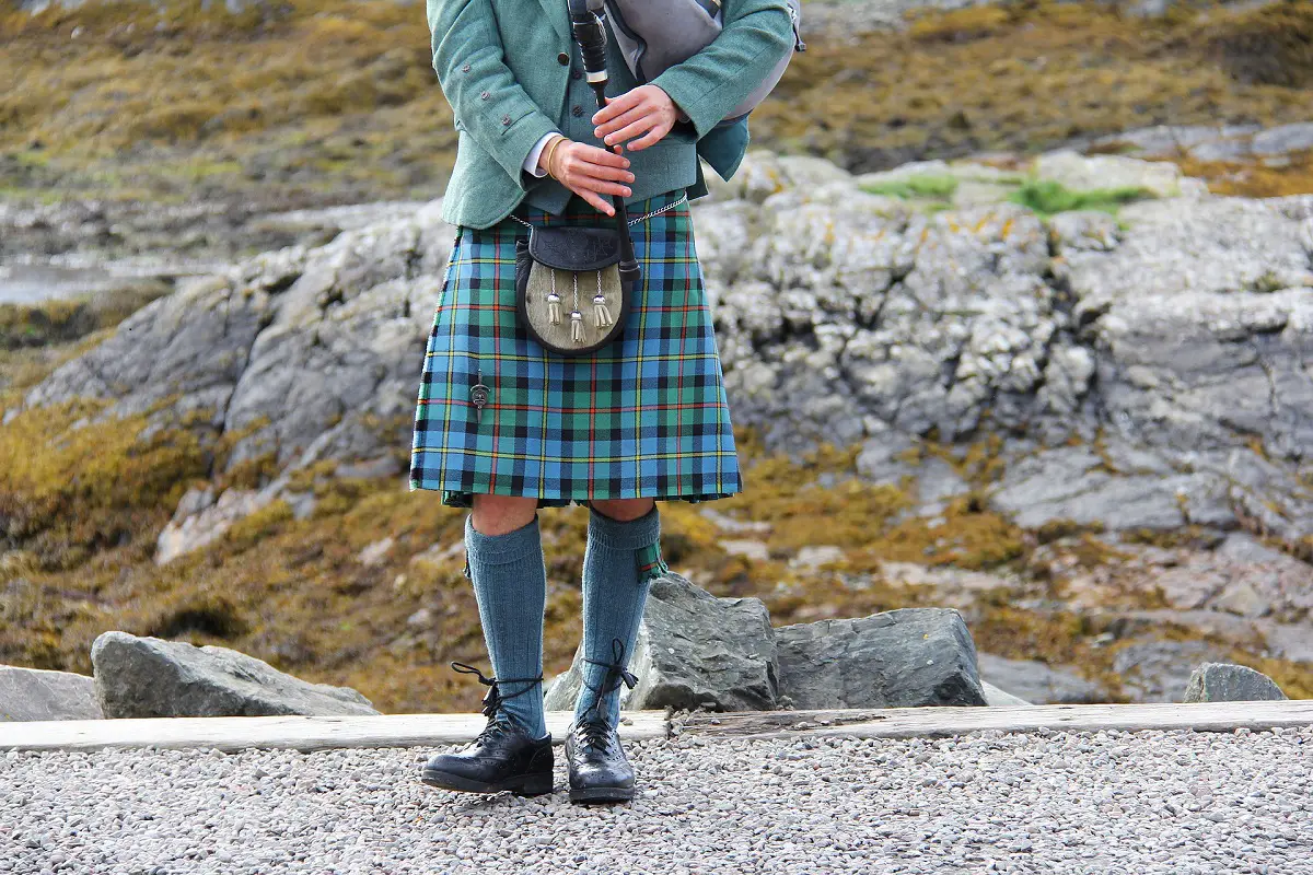 lower half of a man wearing a kilt holding a bagpipe
