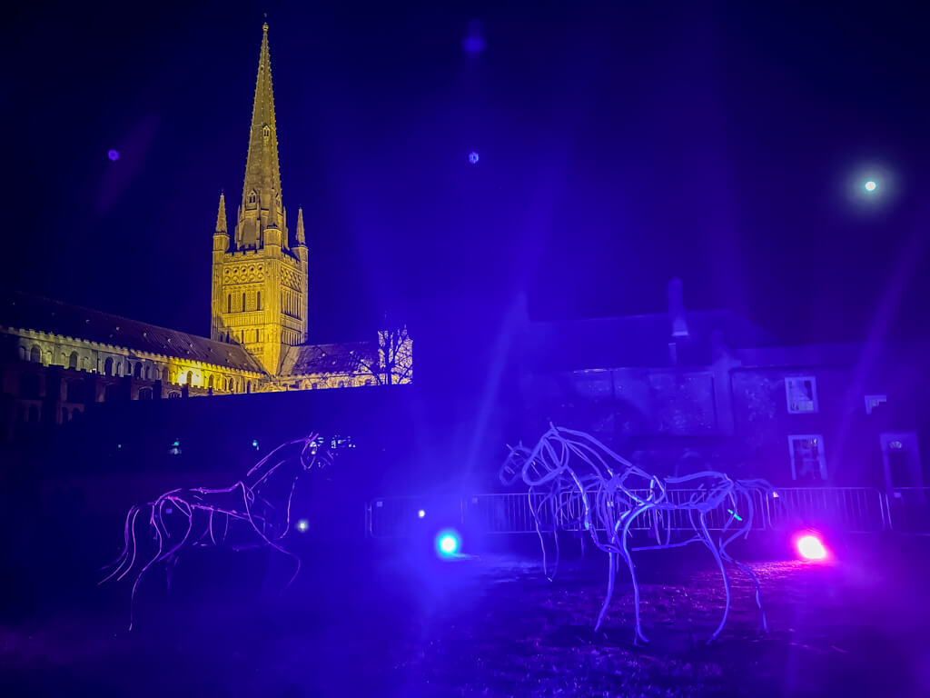 marsh ponies sculptures in front of norwich cathedral with blue and pink lights as part of Love Light Norwich 2022