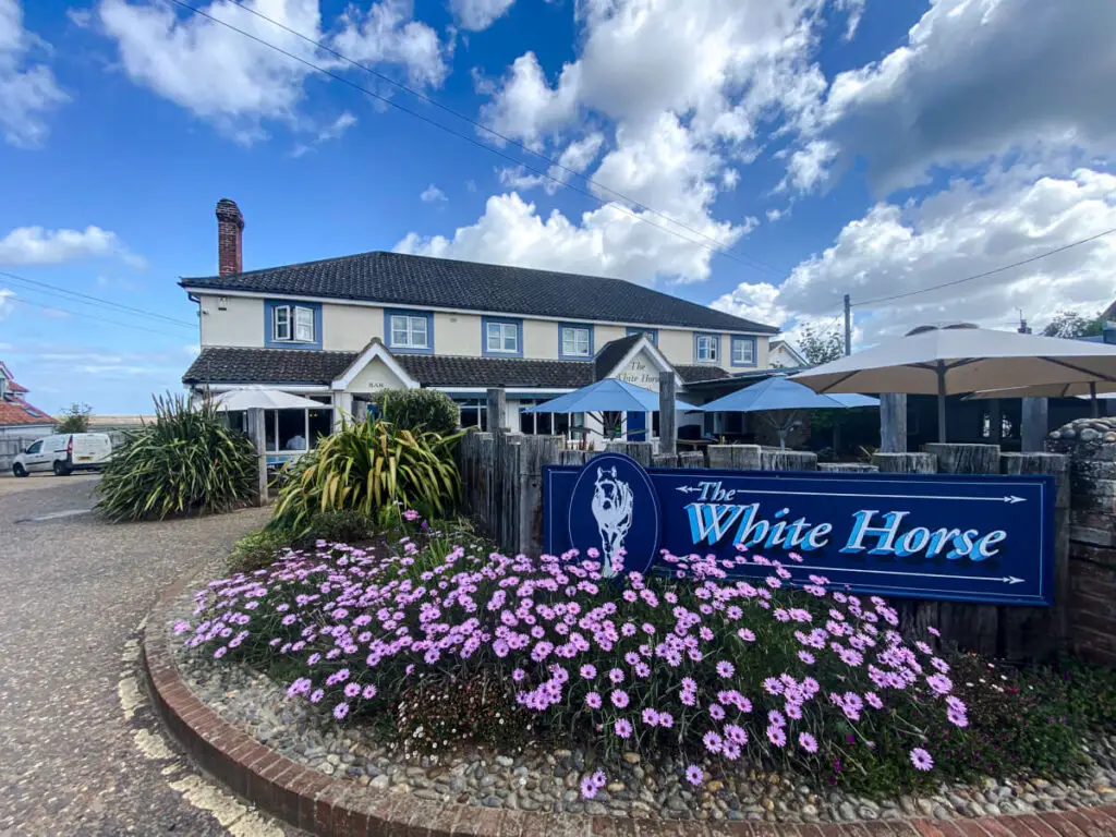 the front of the brancaster white horse with a sign and flowers