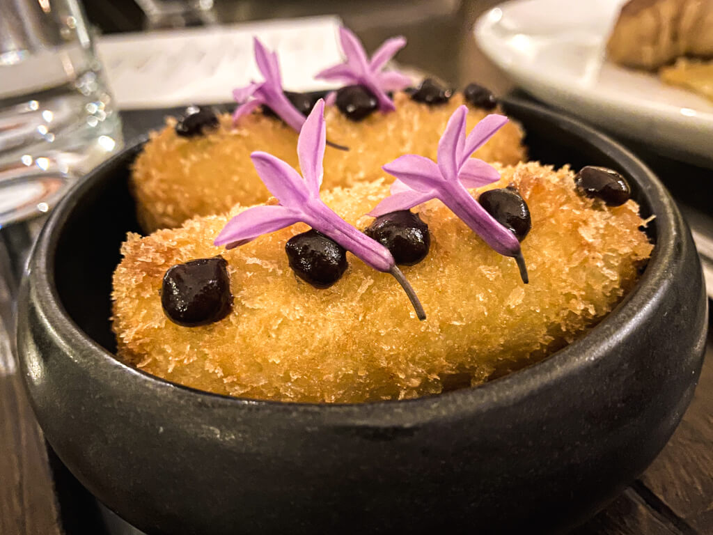 roasted vegetable fritters in a black bowl with purple flowers on top