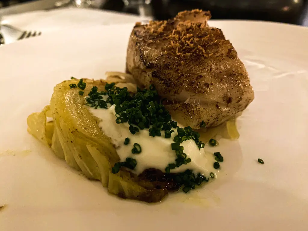 cod served with cabbage artistically presented with a white sauce and chives