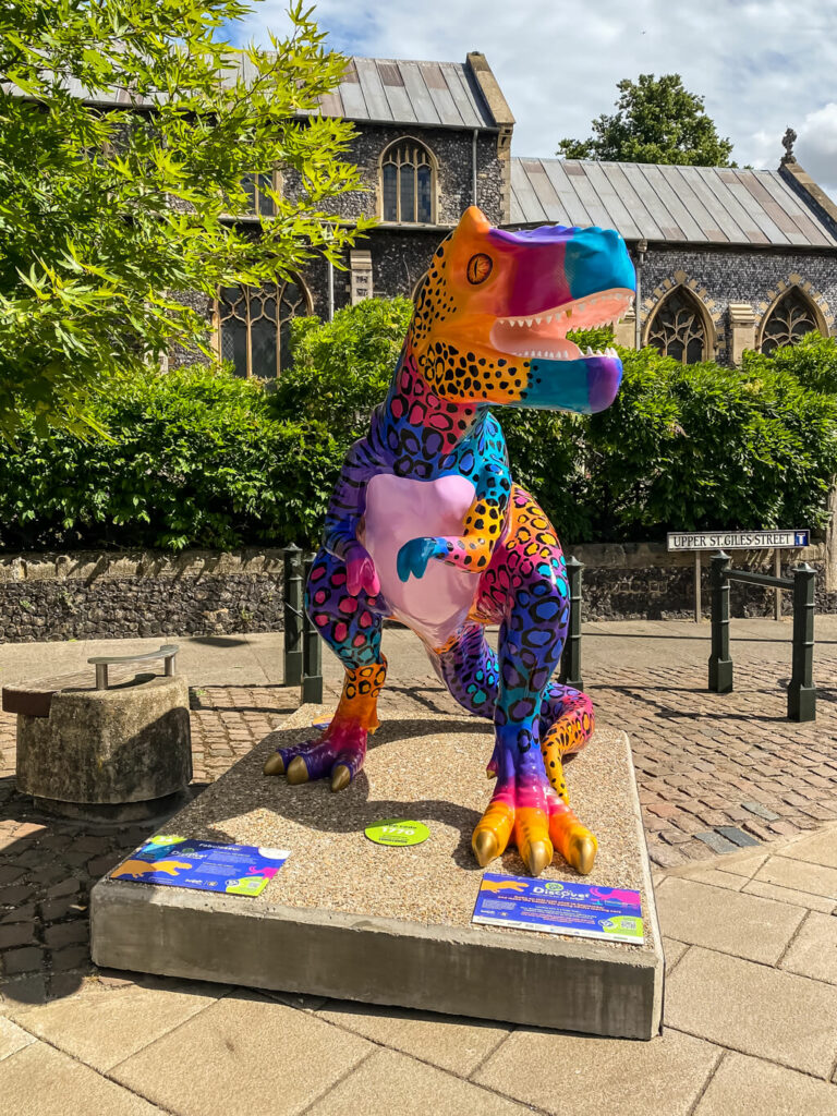 brightly coloured t-rex in front of a church