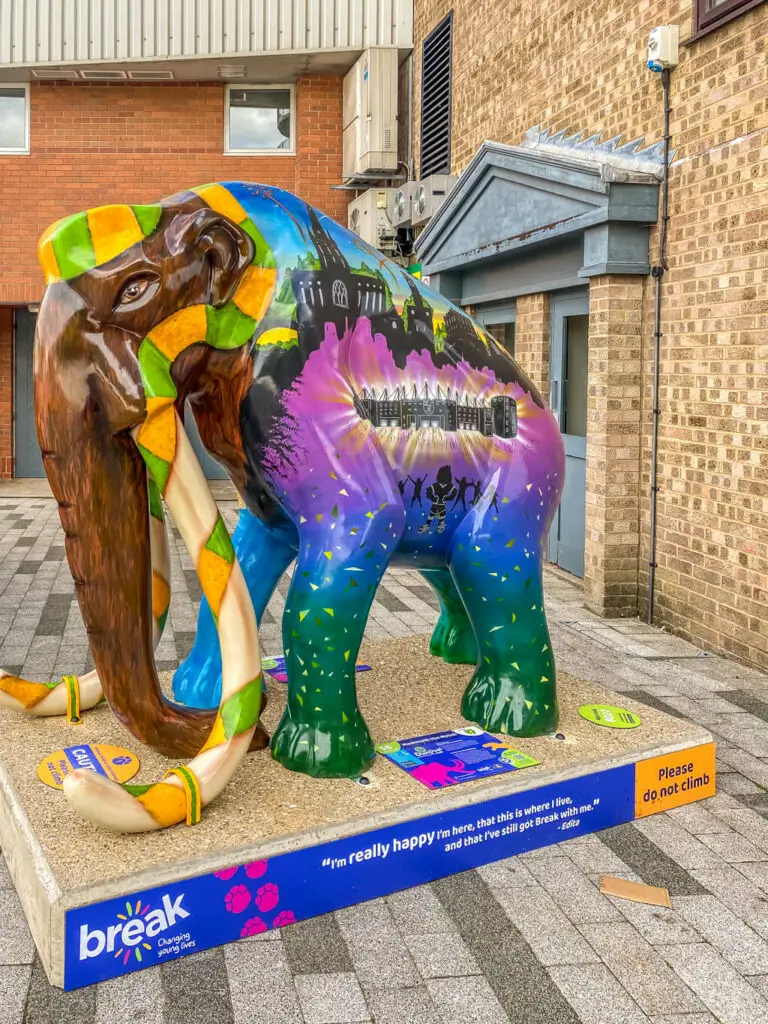 mammoth with yellow and green hat and decoration on tusks with colourful scene painted on body