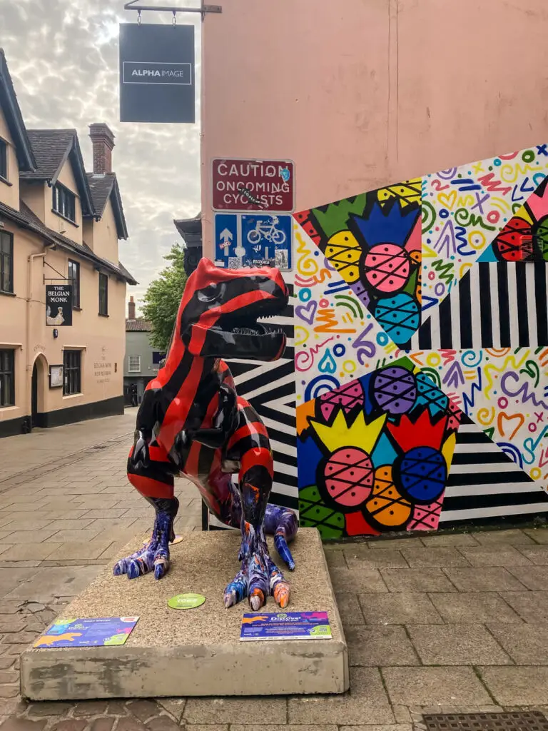 striped dinosaur next to a wall with graffiti