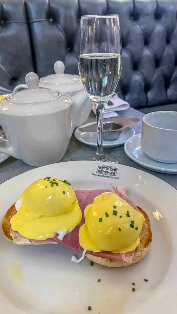 eggs benedict with teapot, glass of prosecco and tea cup in the background