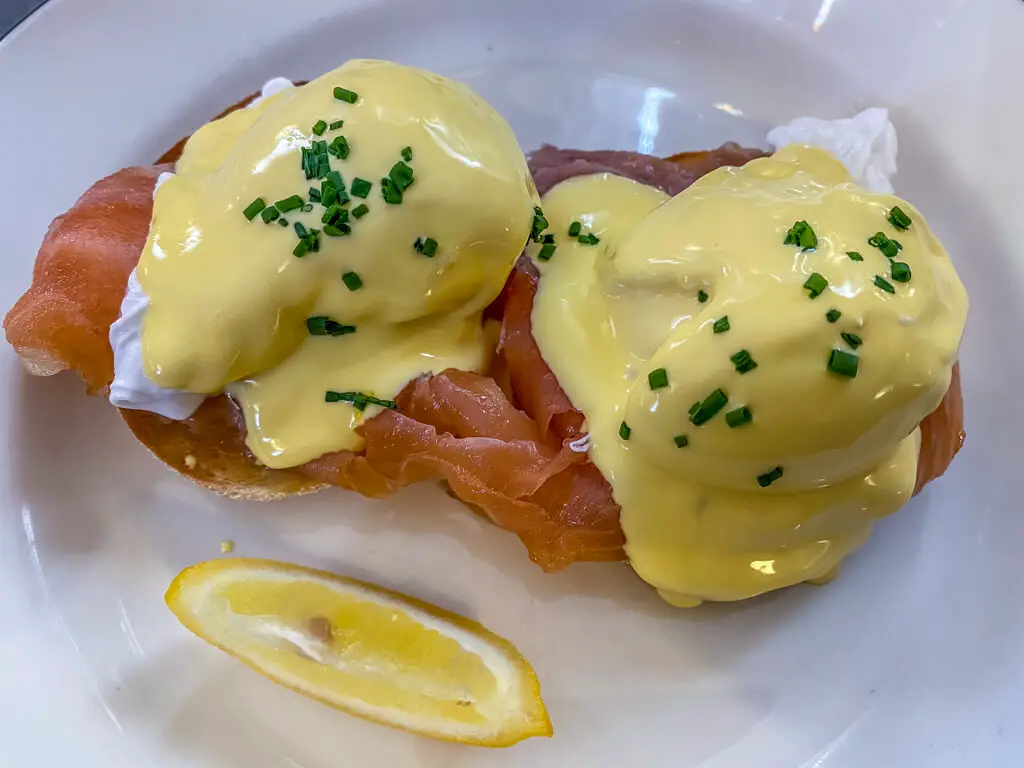 overhead shot of eggs royale (salmon, poached egg, and hollandaise sauce on english muffin) with a small wedge of lemon