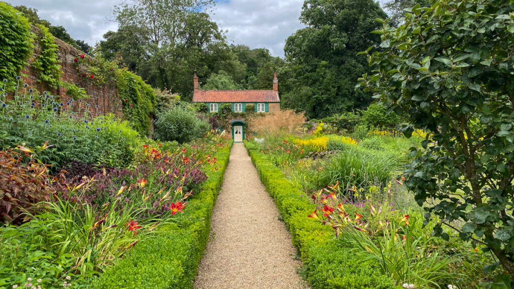 path in walled garden leading to cottage with flowers and plants on both sides.