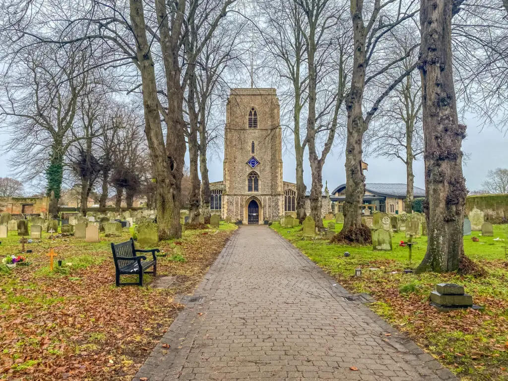 view down a path through trees looking at st andrews church tower in holt