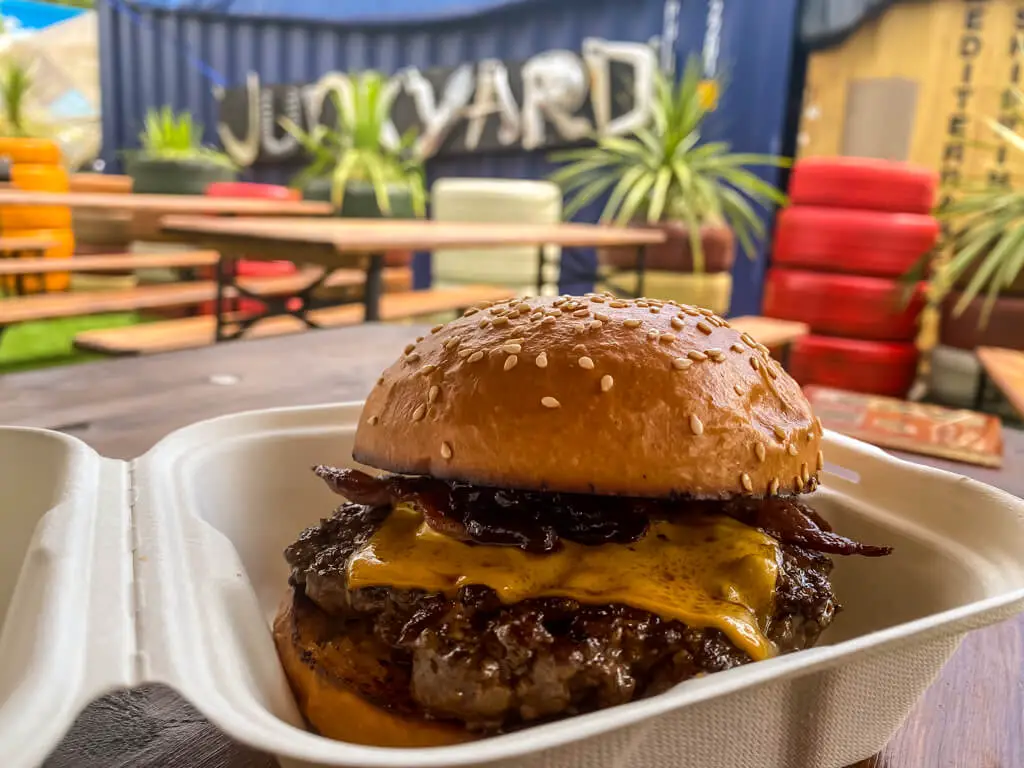 large burger with cheese in plastic container with tables in background