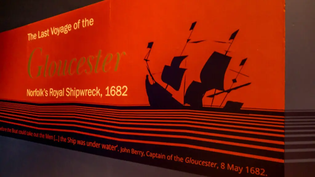 sign for the last voyage of the gloucester exhibition, red background with black sinking warship