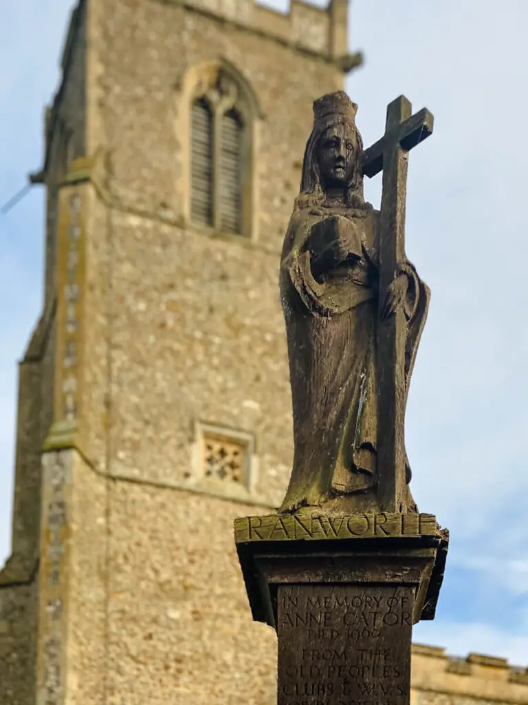 close up of wooden sculpture with Ranworth church tower in the background